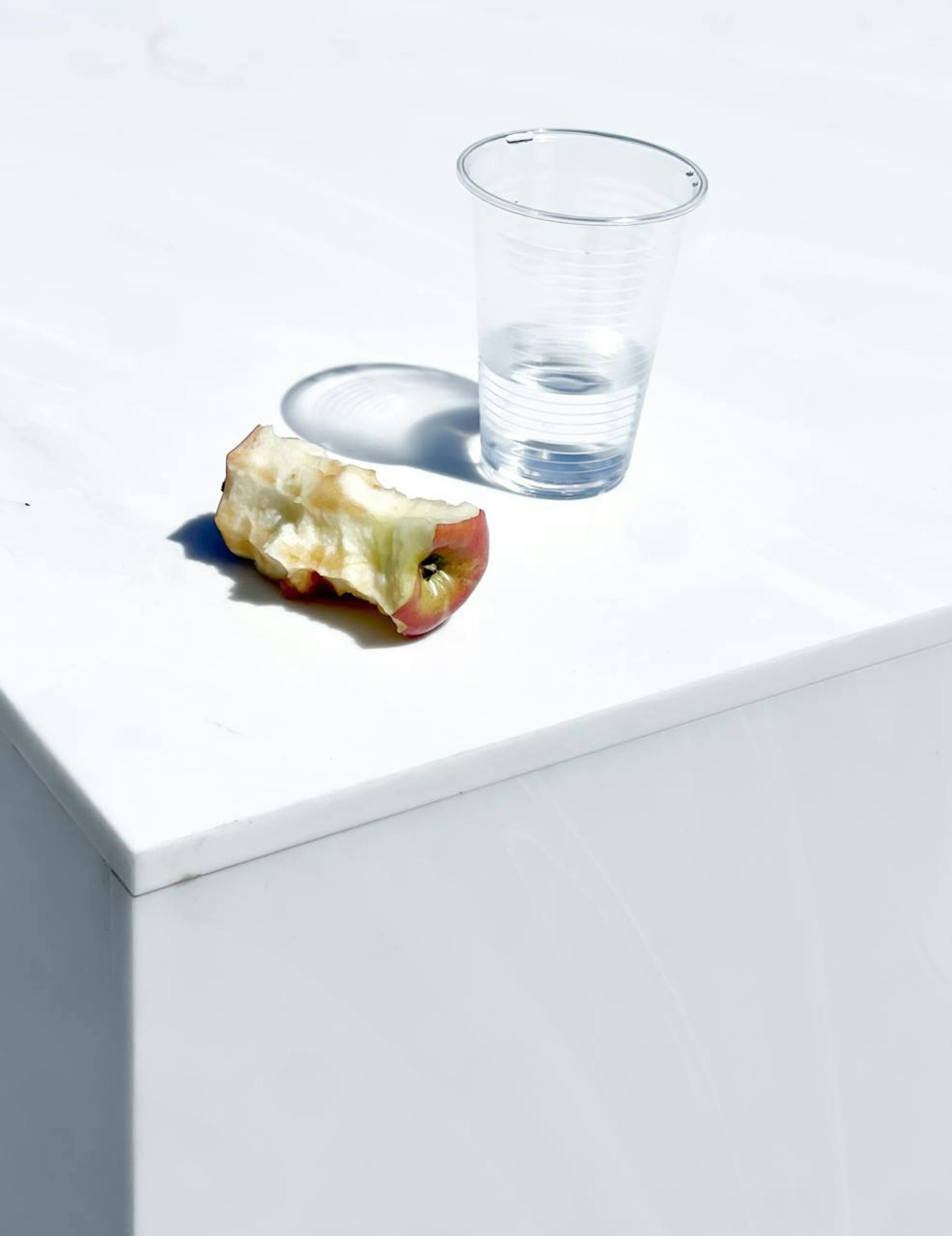 Apple core with almost empty cup on marble stand with shadow